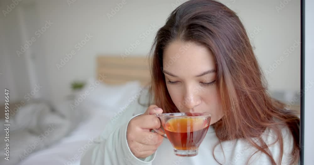 Thoughtful plus size biracial woman having tea in bedroom, looking up, copy space, slow motion Thoughtful plus size biracial woman having tea in bedroom, looking up, copy space, slow motion