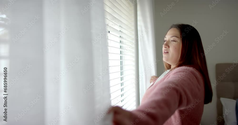 Plus size biracial woman drawing curtains, looking out of bedroom window, copy space, slow motion Plus size biracial woman drawing curtains, looking out of bedroom window, copy space, slow motion