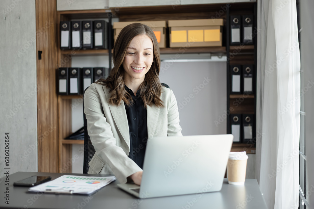 Happy businesswoman using a laptop computer and sitting at desk in office. Happy businesswoman using a laptop computer and sitting at desk in office.