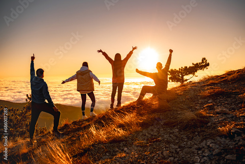 Group of happy friends are standing at mountain top and greeting sunrise or sunset above clouds photo