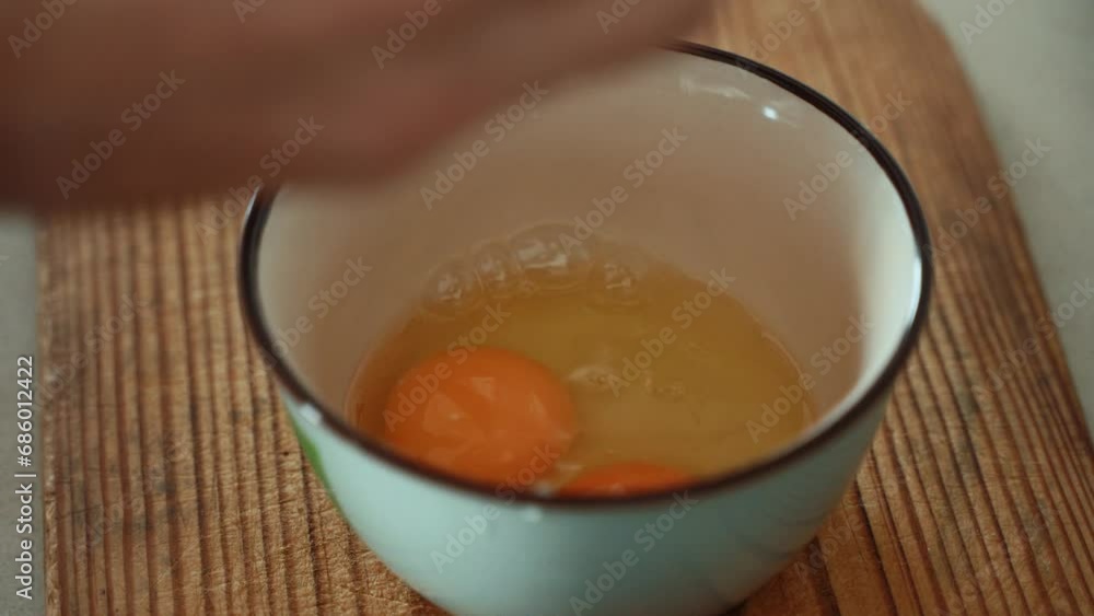 A close up shot of a breaking raw egg into a white bowl, brown wooden plate, 4K video A close up shot of a breaking raw egg into a white bowl, brown wooden plate, 4K video
