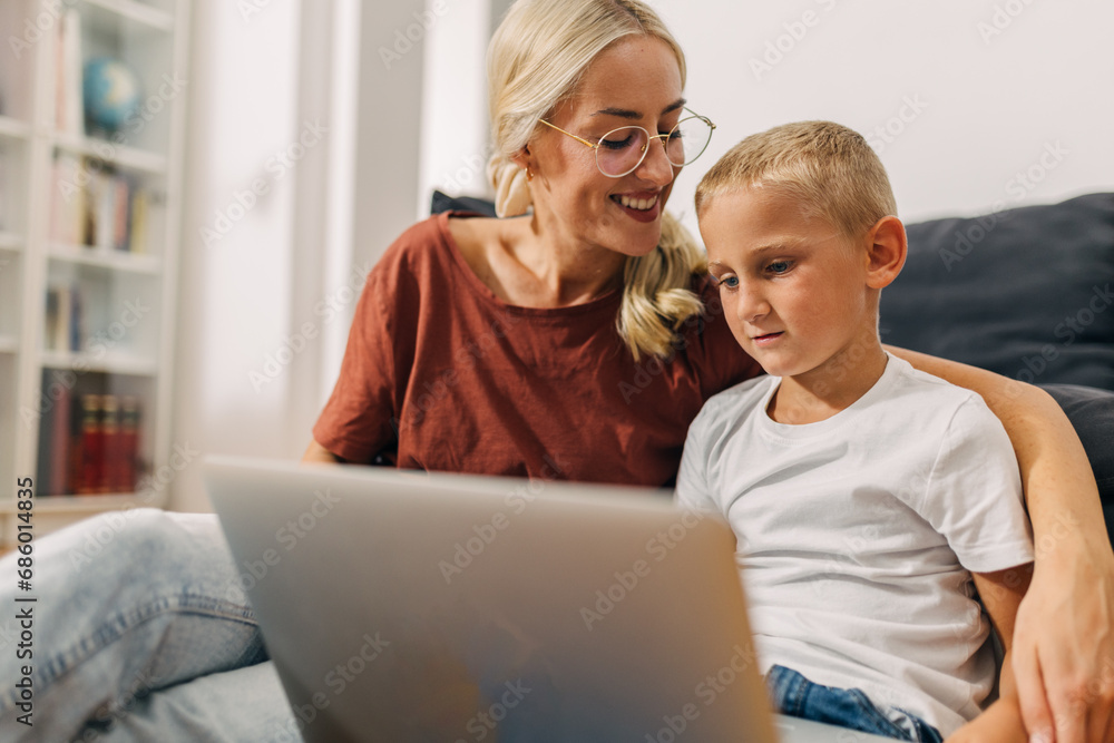 Happy mother sitting next to her son while he uses laptop. Happy mother sitting next to her son while he uses laptop.