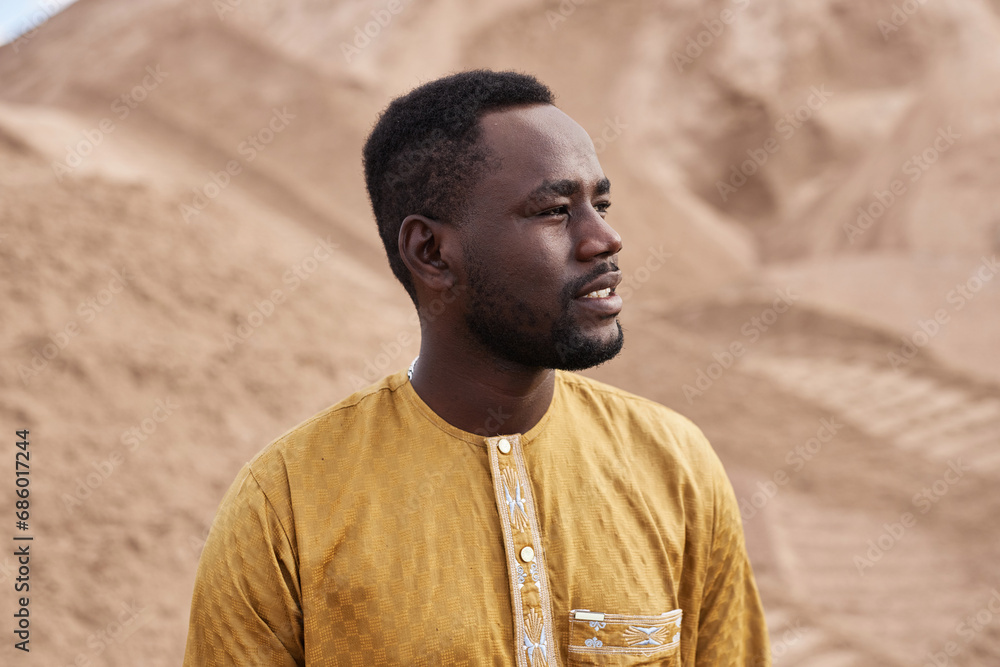 Side view portrait of Black man wearing traditional clothing looking away in desert, copy space Side view portrait of Black man wearing traditional clothing looking away in desert, copy space