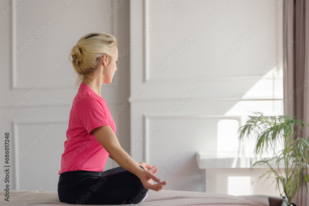 Young calm focused young woman doing pilates breathing exercises while sitting in a bright room