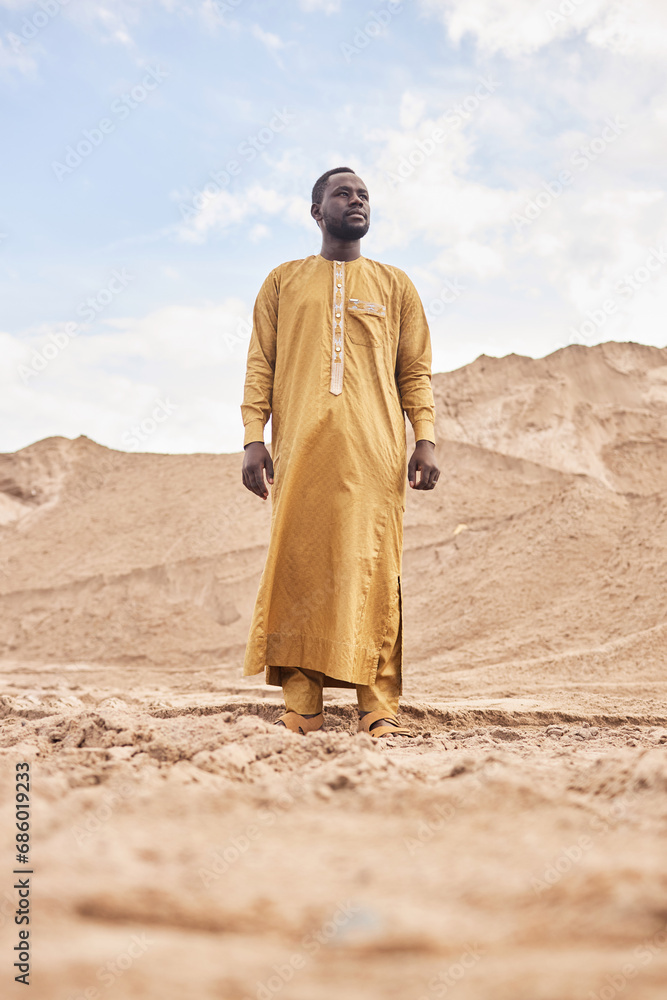 Naklejka premium Dramatic full length portrait of African American man wearing traditional long kaftan in desert landscape
