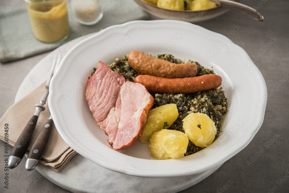 Oldenburger Grünkohl mit geräucherter Kohlwurst, Pinkel, Kassler Nacken, Kartoffeln, Senf, Petersilie auf Teller und hell grau Stein Hintergrund Oldenburger Grünkohl mit geräucherter Kohlwurst, Pinkel, Kassler Nacken, Kartoffeln, Senf, Petersilie auf Teller und hell grau Stein Hintergrund