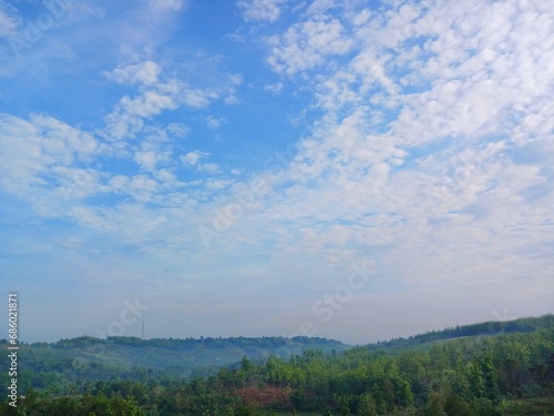 The view of the plantations is green and beautiful, there are blue clouds. See the view of the hills with blue clouds.