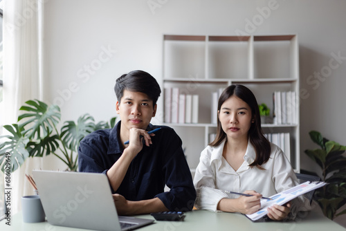 Two asian young businesswoman and man using laptop with documents in office working space.
