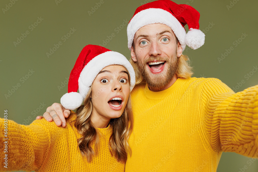 Close up merry young couple two friends man woman wear sweater Santa hat posing doing selfie shot pov on mobile cell phone isolated on plain green background. Happy New Year Christmas holiday concept. Close up merry young couple two friends man woman wear sweater Santa hat posing doing selfie shot pov on mobile cell phone isolated on plain green background. Happy New Year Christmas holiday concept.