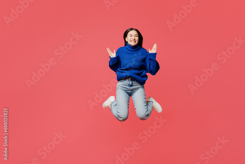 Full body young happy woman of Asian ethnicity she wear blue sweater casual clothes jump high look camera spread hands isolated on plain pastel light pink background studio portrait Lifestyle concept