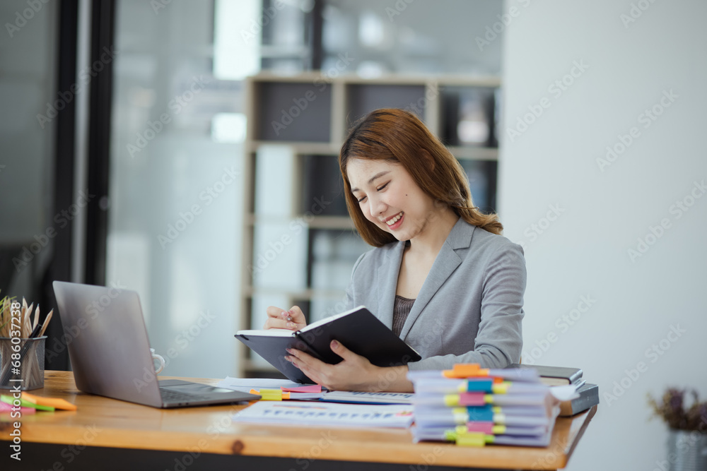 Happy young asian businesswoman with laptop sitting at workplace in modern office. Happy young asian businesswoman with laptop sitting at workplace in modern office.