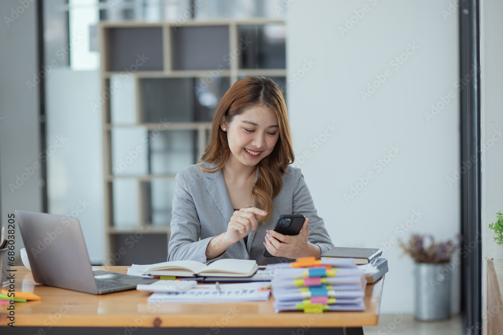 Accounting asian woman use smartphone and laptop at office desk in office, Accounting businesswoman online working concept. Accounting asian woman use smartphone and laptop at office desk in office, Accounting businesswoman online working concept.