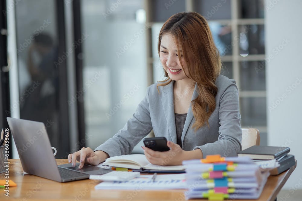 Accounting asian woman use smartphone and laptop at office desk in office, Accounting businesswoman online working concept. Accounting asian woman use smartphone and laptop at office desk in office, Accounting businesswoman online working concept.