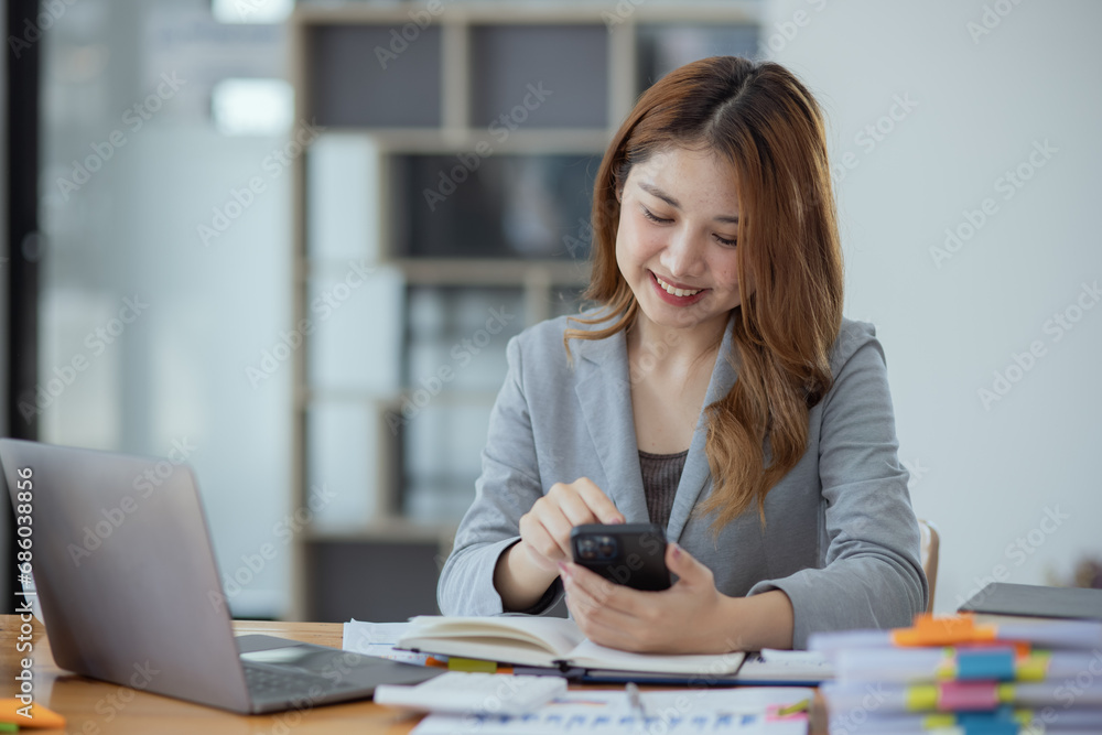 Accounting asian woman use smartphone and laptop at office desk in office, Accounting businesswoman online working concept.