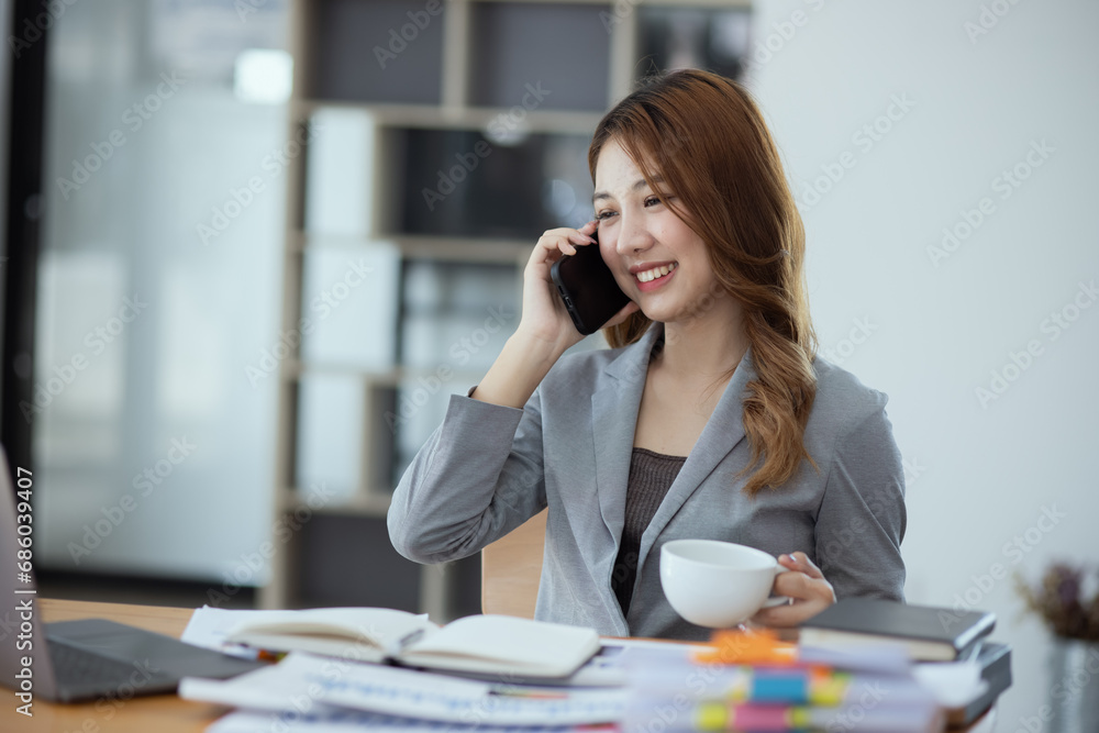 Accounting asian woman use smartphone and laptop at office desk in office, Accounting businesswoman online working concept. Accounting asian woman use smartphone and laptop at office desk in office, Accounting businesswoman online working concept.