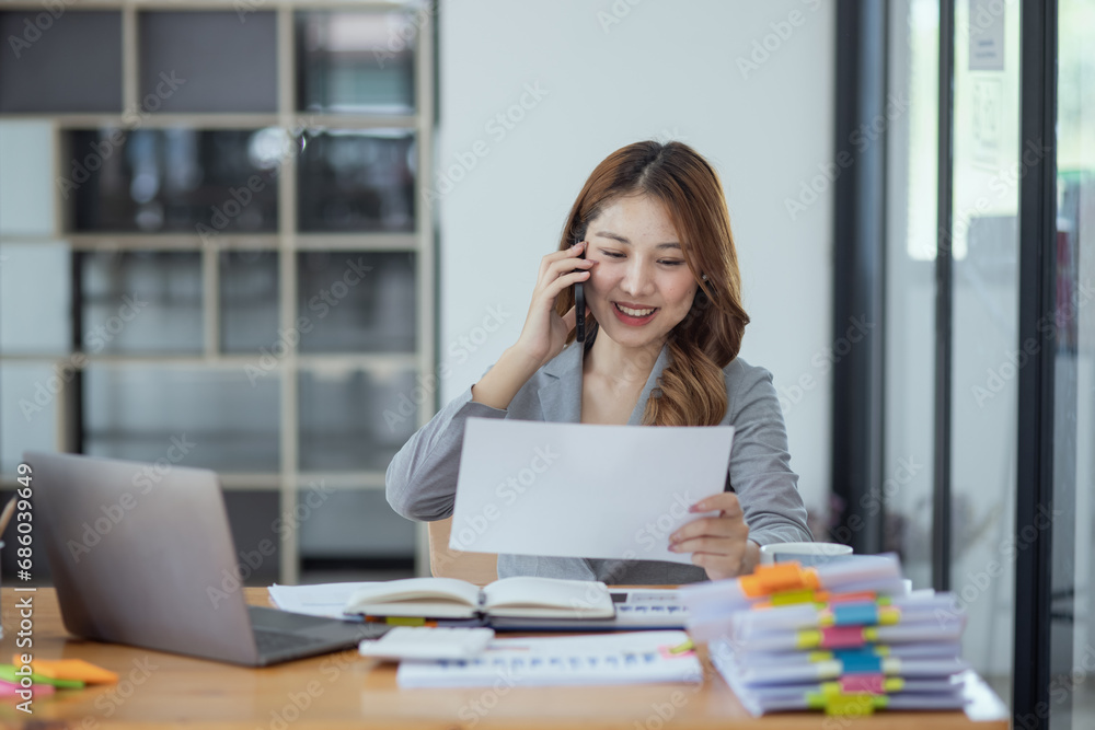 Accounting asian woman use smartphone and laptop at office desk in office, Accounting businesswoman online working concept. Accounting asian woman use smartphone and laptop at office desk in office, Accounting businesswoman online working concept.