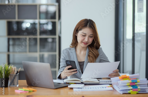 Accounting asian woman use smartphone and laptop at office desk in office, Accounting businesswoman online working concept.