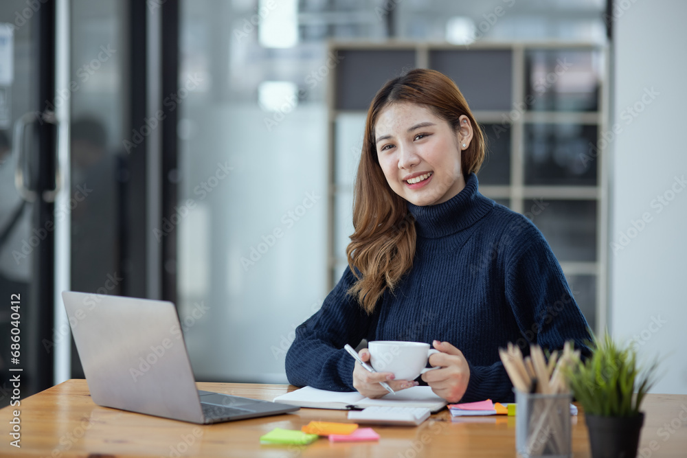 Happy young asian businesswoman with laptop sitting at workplace in modern office. Happy young asian businesswoman with laptop sitting at workplace in modern office.
