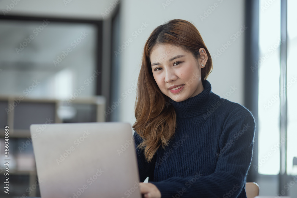 Happy young asian businesswoman with laptop sitting at workplace in modern office. Happy young asian businesswoman with laptop sitting at workplace in modern office.