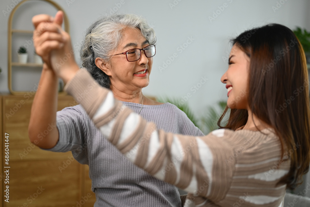 Happy gray haired middle age mother dancing with grown up daughter in living room Happy gray haired middle age mother dancing with grown up daughter in living room