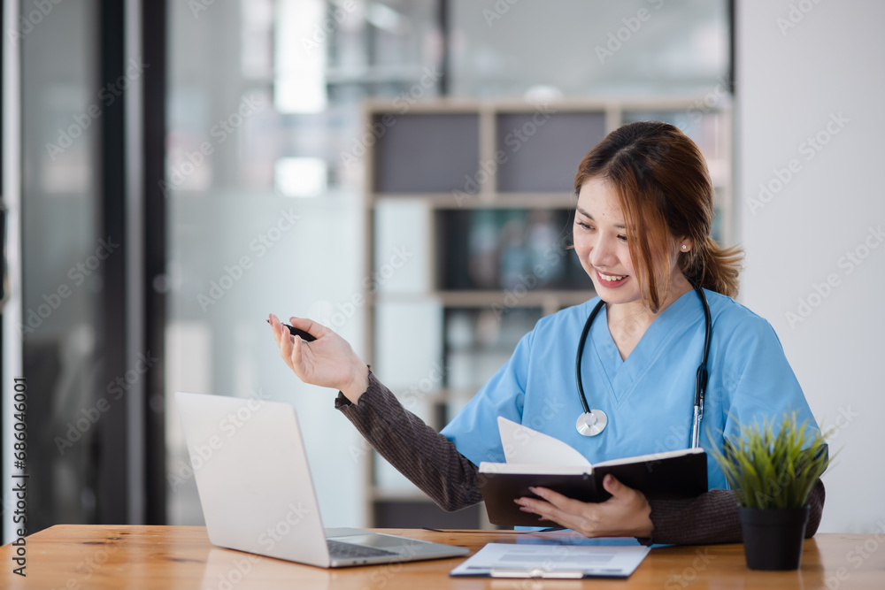 Asian female doctor working with a patient clipboard and digital laptop sitting at desk in hospital, Medicine and healthcare concept. Asian female doctor working with a patient clipboard and digital laptop sitting at desk in hospital, Medicine and healthcare concept.