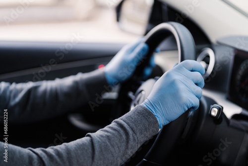 Driver's hands on a steering wheel, wearing blue protective gloves for hygiene © VK Studio