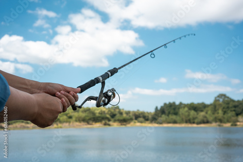 Woman holding fishing rod in her hands into the lake on sunny day.
