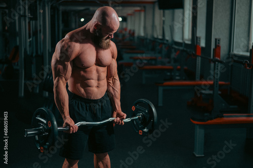 Caucasian bald topless man doing an exercise with a barbell in the gym. Bicep curls with weights. photo