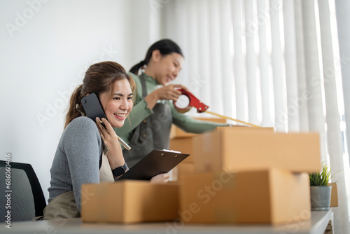 Small business SME owner, Two young Asian business owner woman prepare parcel box and check online orders of product for deliver to customer, packaging, Shopping Online concept © Natee Meepian
