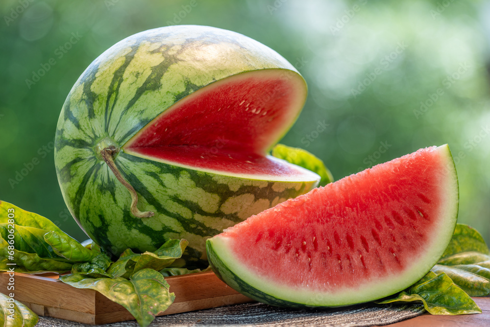 Watermelon in wooden basket on wooden table in garden, Fresh Watermelon with slices on blurred greenery background.