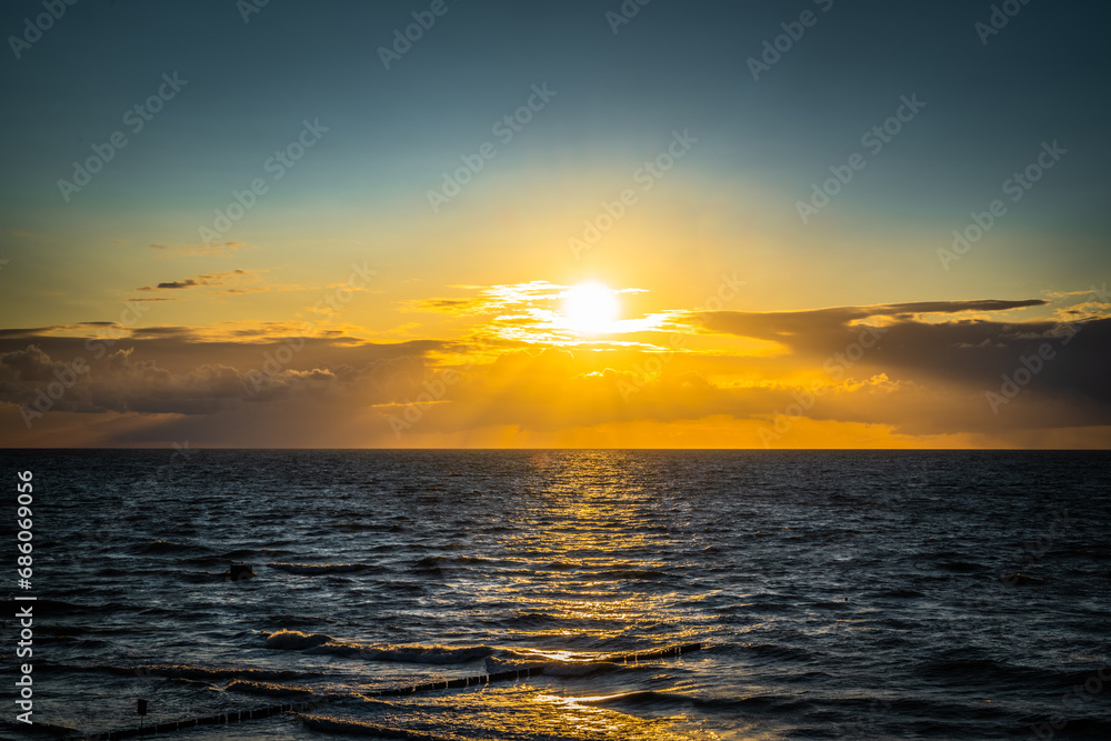 Obraz premium The sunset over the Baltic Sea paints the sky in shades of orange and pink, reflecting golden reflections on the surface of the sea, creating a magical and peaceful landscape.