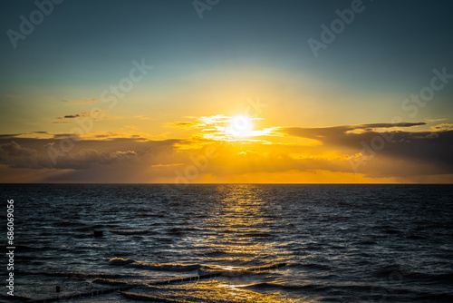 The sunset over the Baltic Sea paints the sky in shades of orange and pink, reflecting golden reflections on the surface of the sea, creating a magical and peaceful landscape.