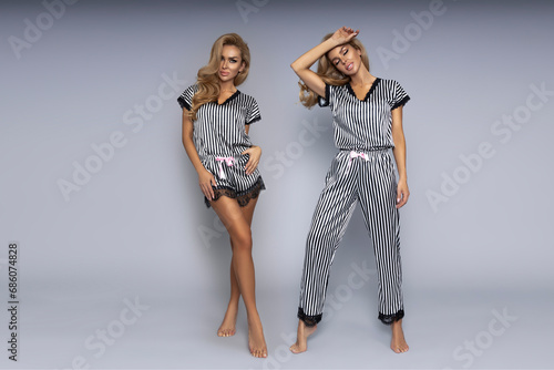 Beautiful woman in striped satin pajamas, posing sensually on a gray background in the studio.