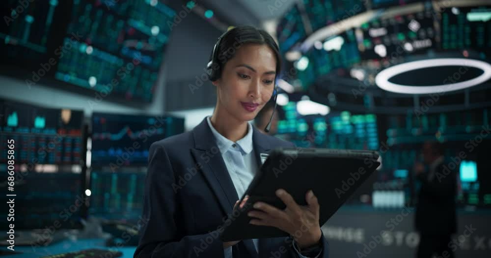 Portrait of a Beautiful Asian Female Working in an International Stock Exchange Hall: Specialist Wearing Headphones and Using Tablet Computer, Successful Trader Looking at Camera and Smiling Portrait of a Beautiful Asian Female Working in an International Stock Exchange Hall: Specialist Wearing Headphones and Using Tablet Computer, Successful Trader Looking at Camera and Smiling