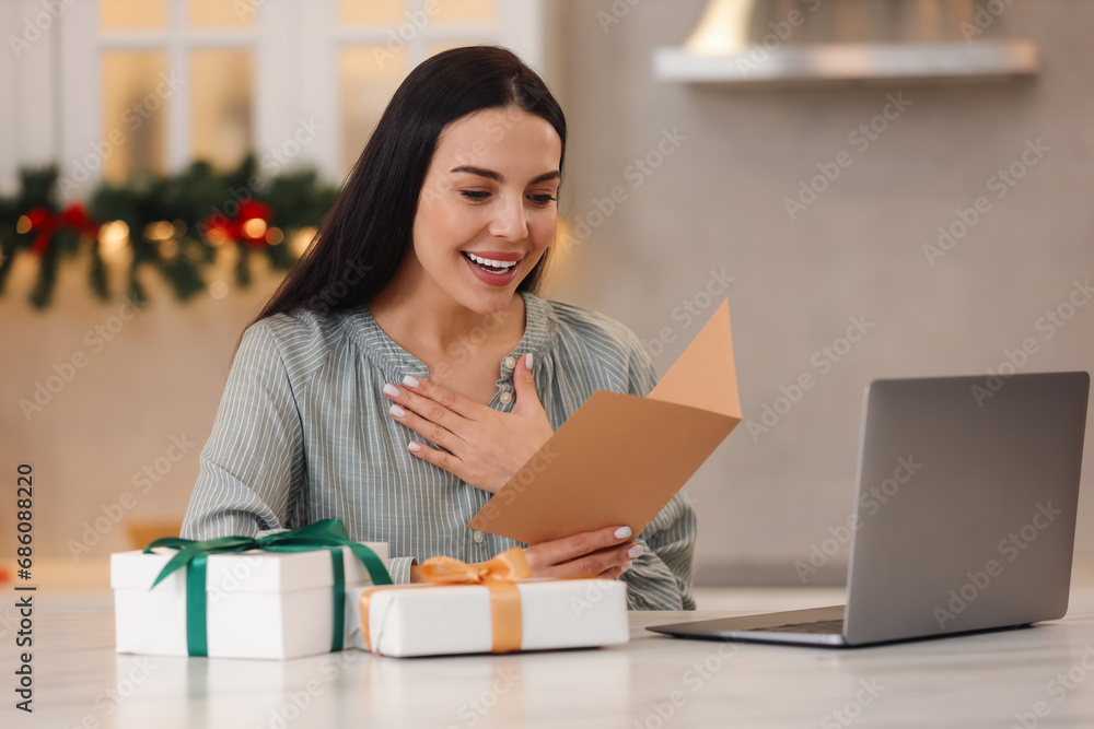 Celebrating Christmas online with exchanged by mail presents. Smiling woman reading greeting card and gifts during video call at home Celebrating Christmas online with exchanged by mail presents. Smiling woman reading greeting card and gifts during video call at home