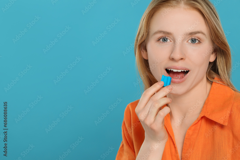 Woman putting bubble gum into mouth on light blue background. Space for text Woman putting bubble gum into mouth on light blue background. Space for text