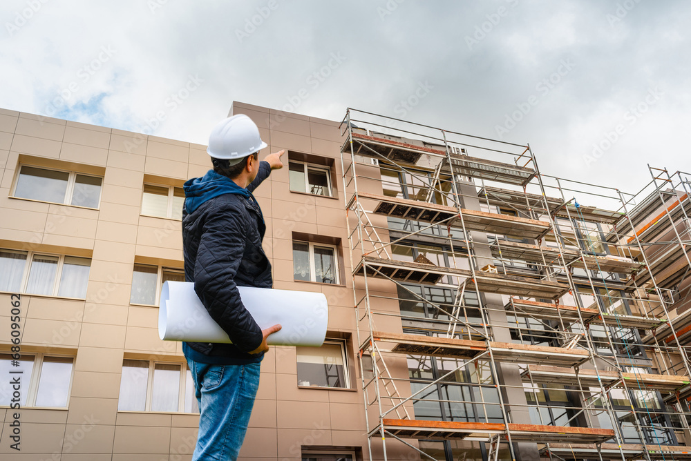 Engineering Consulting Engineer showing window at construction site holding blueprint in his hand.Building inspector.Construction site check drawing and business workflow of new building.