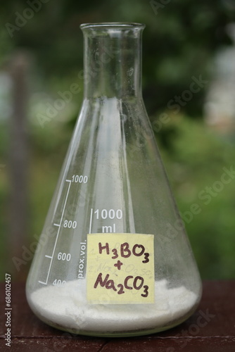 Fotografie Reagents for preparing fireproof coating for wood: boric acid and sodium carbonate in a large conical flask