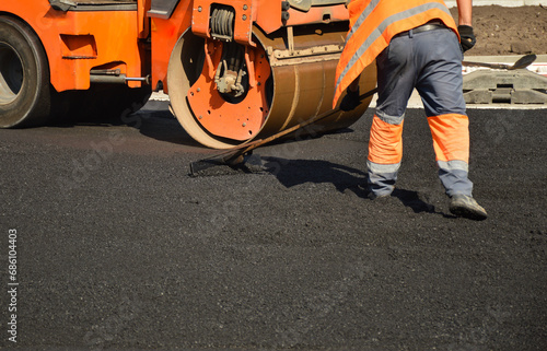 a worker levels the asphalt in front of a road roller