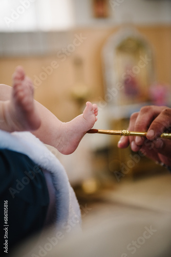 Anointing at baptism. Closeup of tiny baby feet, the sacrament of baptism ceremony. Godmother holds the child in his arms. Priest and godfather stretch hands to child legs. Temple, Orthodoxy.