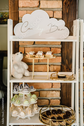 Candy bar at a child's birthday party or baptism. Delicious reception luxury ceremony. Table with sweets, candies, desserts, ice cream, and macaroons. Table with soft toys bear.