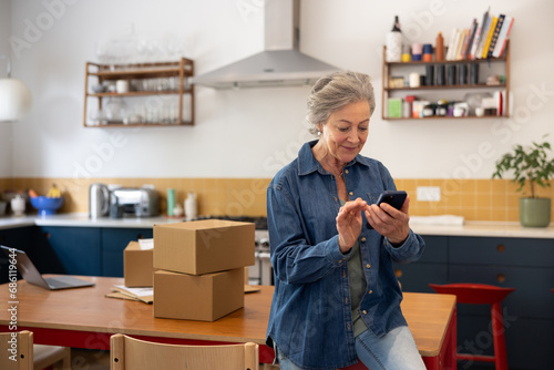 Senior female businesswoman packing orders and using a smartphone working from home photo
