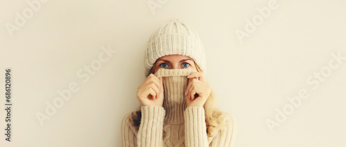 Winter portrait of woman freezing trying to warm up wearing warm soft knitted clothes, hat and sweater on beige studio background photo