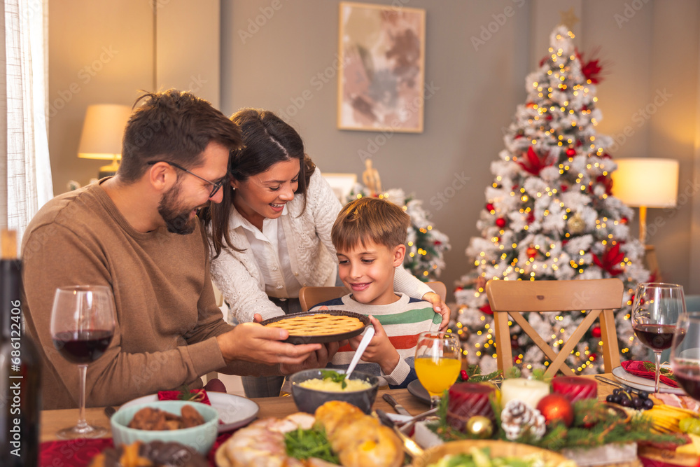 Mother and father offering apple pie to son during Christmas dinner at home