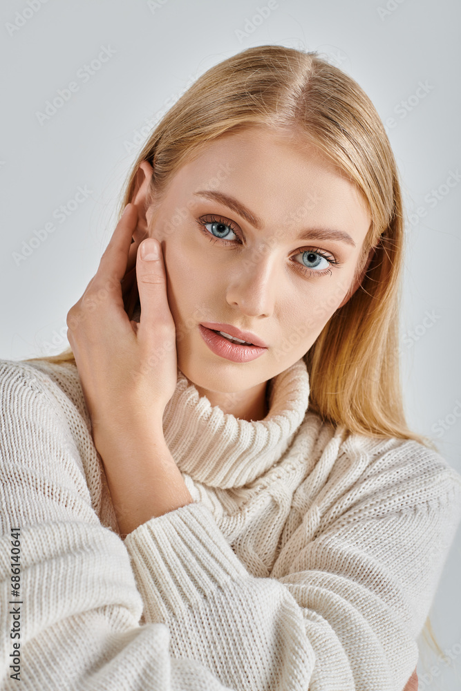 portrait of sensual blonde woman in natural makeup and white winter sweater touching face on grey portrait of sensual blonde woman in natural makeup and white winter sweater touching face on grey