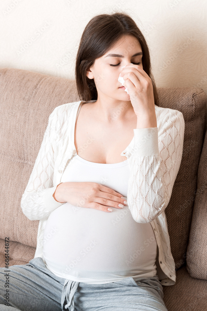 Sick pregnant woman blowing nose into tissue at home Healthy millennial healthcare concept Sick pregnant woman blowing nose into tissue at home Healthy millennial healthcare concept