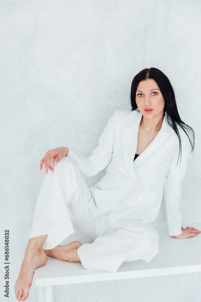 Fashionable brunette woman in white suit sitting on table