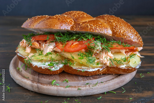 Challah Sandwich with grilled salmon, boiled potato, fresh tomatoes and fennel on dark background.