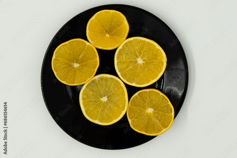 Photo of sliced oranges in a black plate on a white background Photo of sliced oranges in a black plate on a white background