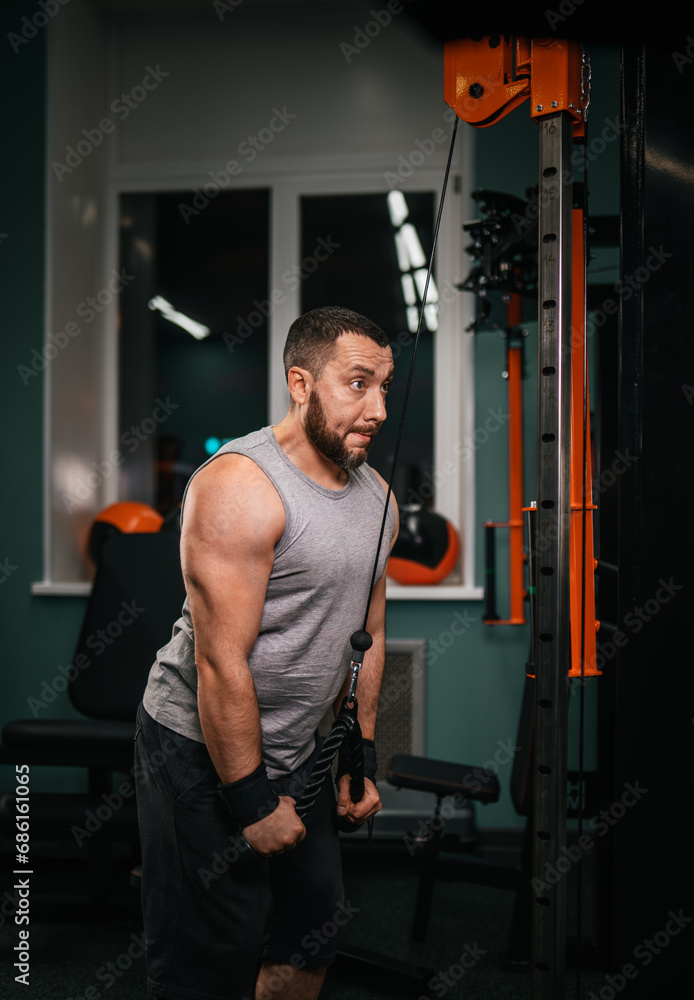 A swarthy man with a beard with effort performs a triceps exercise pulling the block to the bottom in the gym. A swarthy man with a beard with effort performs a triceps exercise pulling the block to the bottom in the gym.